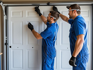 Two technicians in blue uniforms installing a new white garage door in a residential garage in Fountain Valley, CA